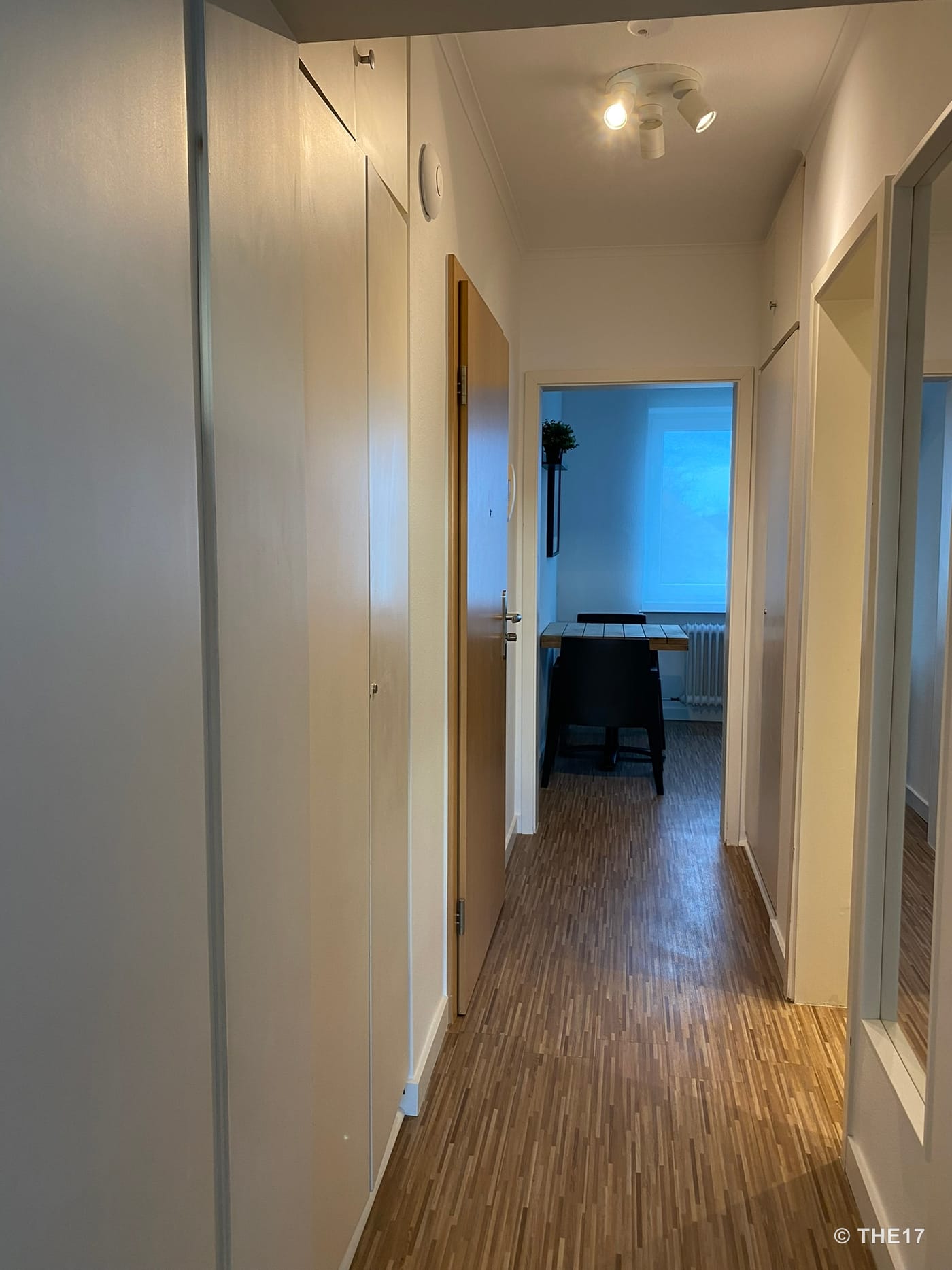 Hallway with wooden floor, white walls, built-in closets, and view into a room with a table and chairs.