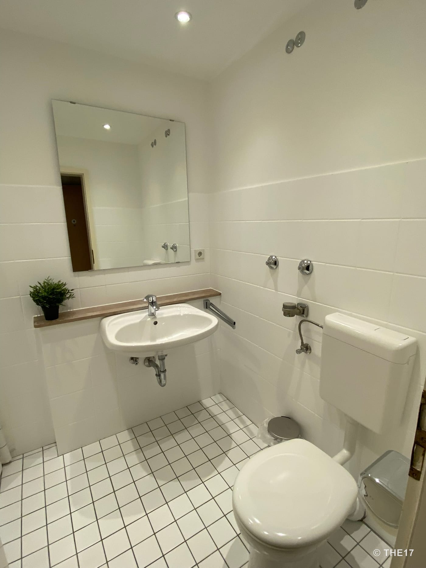 Kleines weiß gefliestes Badezimmer mit Waschbecken, großem Spiegel und Toilette.