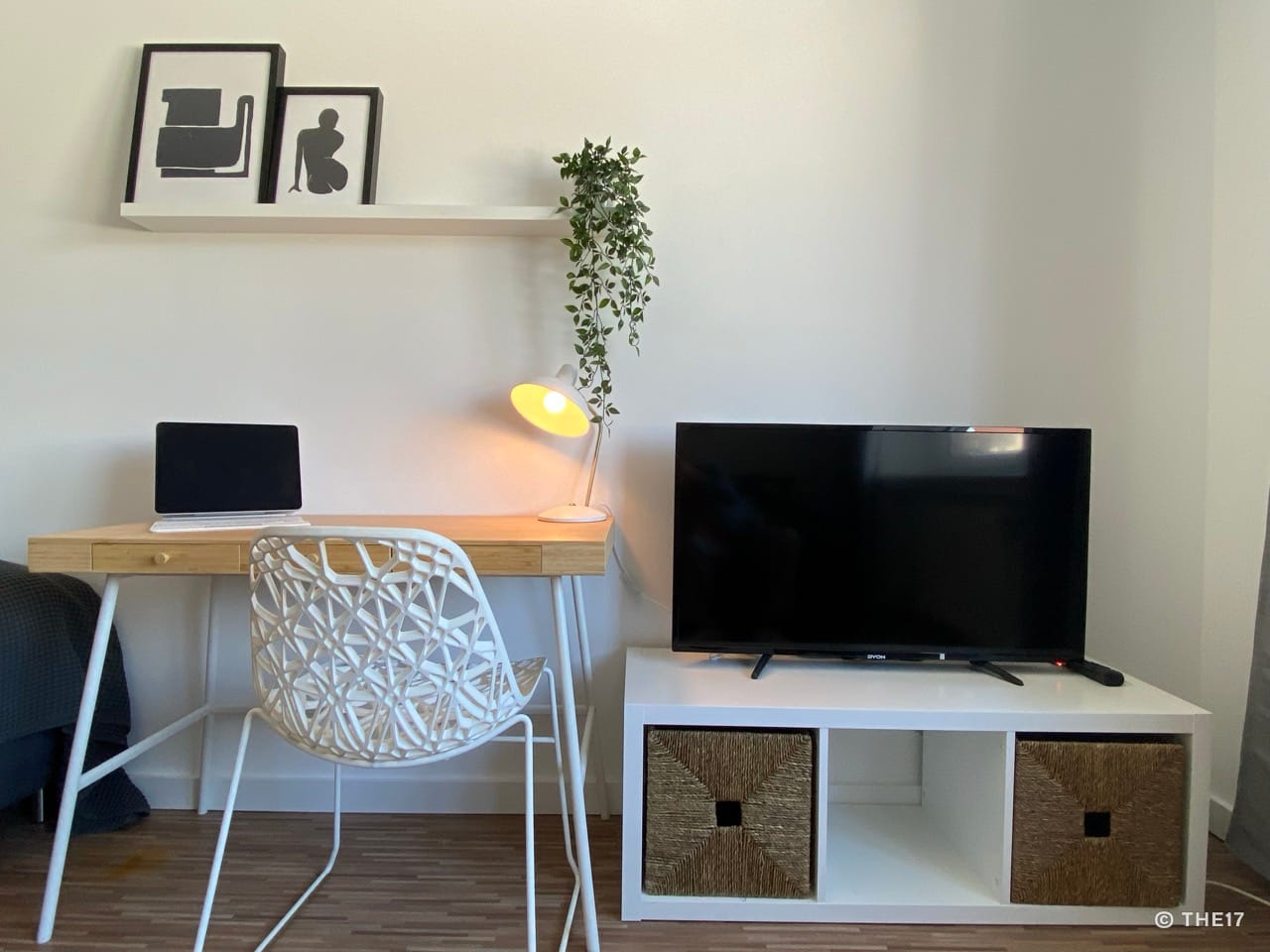 Weißer Schreibtisch mit Laptop und Lampe, weiße Designer-Stuhl, TV auf weißem Lowboard mit zwei Körben.