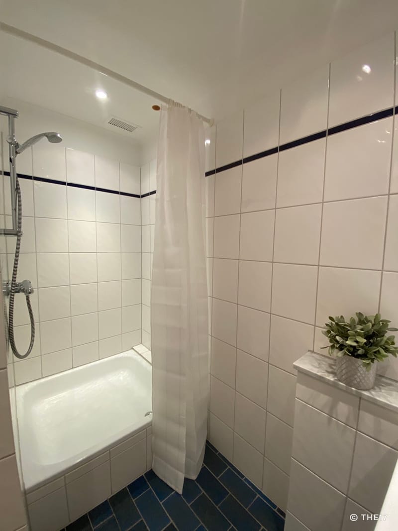 Small shower with white tiles and dark blue floor, shower curtain, and small plant on ledge.