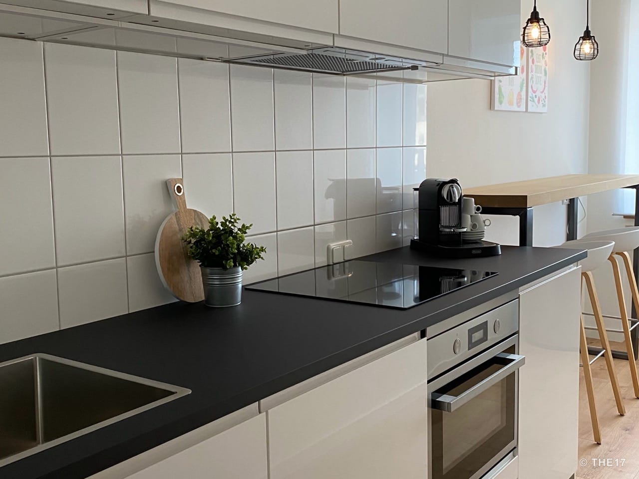 Moderne Küche mit schwarzer Arbeitsfläche, Induktionskochfeld, Kaffeemaschine und Holzbar mit Hockern.
