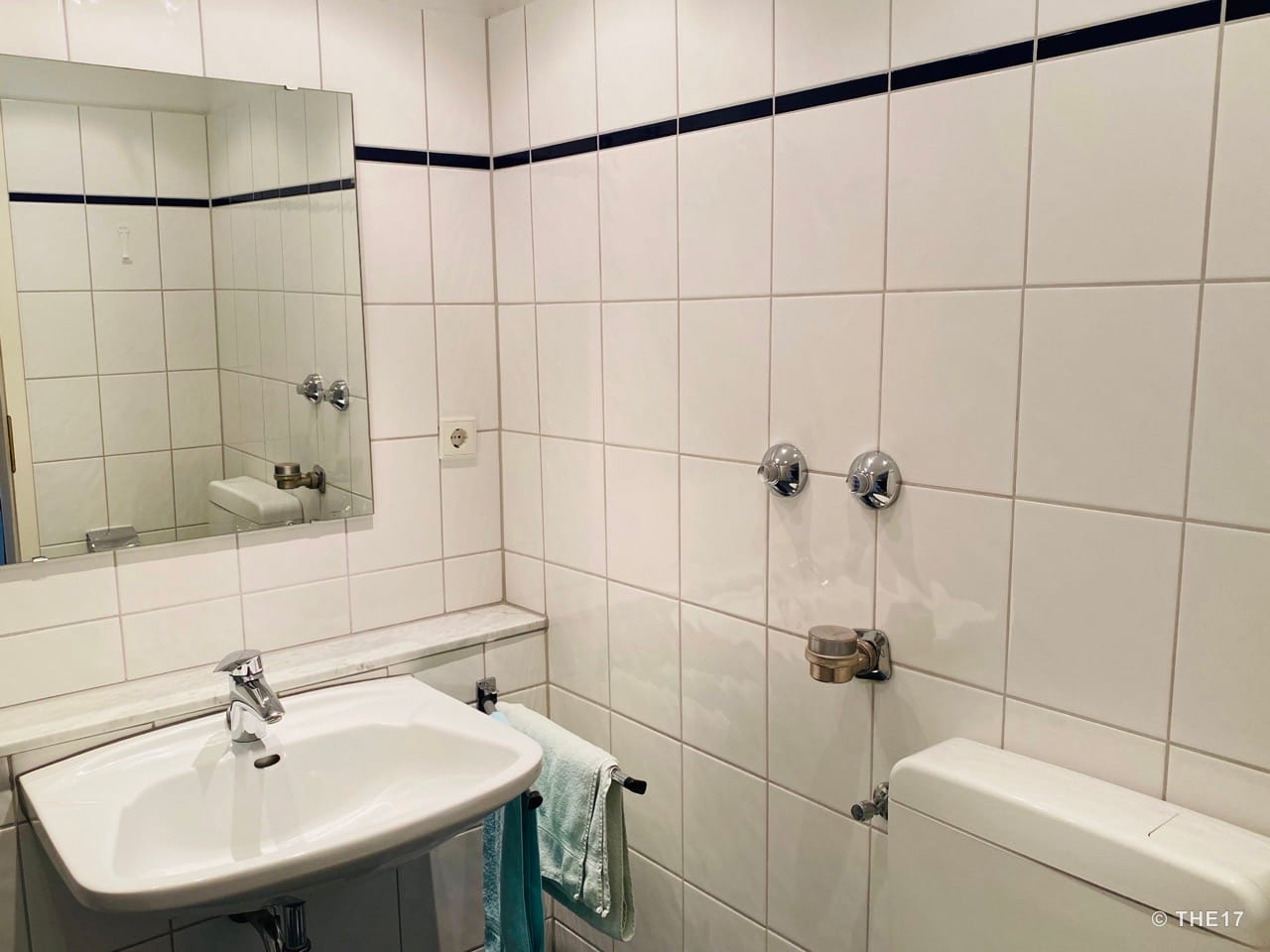 Bathroom with white tiles, rectangular sink, large mirror, and two towels hanging on a rail.