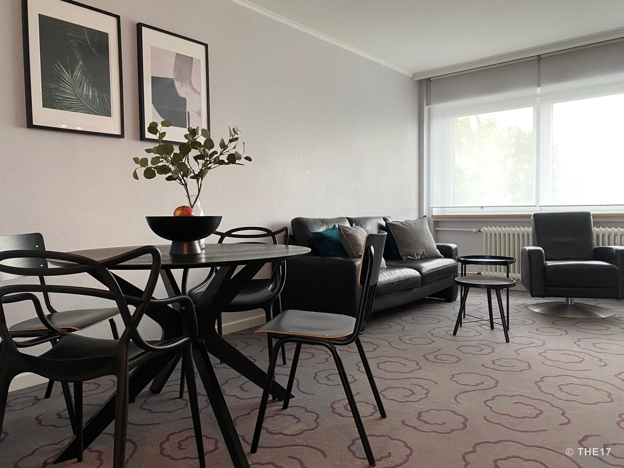 Moderner Wohnbereich mit Ledersofa, Sessel, runden Couchtischen, einem schwarzen Esstisch mit Stühlen und zwei Wandbildern.