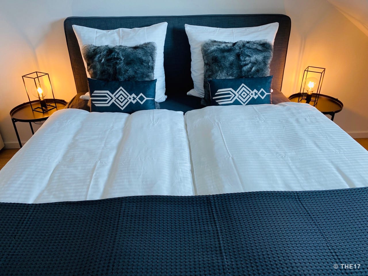 Double bed with dark gray headboard, white bedding, black decorative pillows, and two bedside tables with lamps.