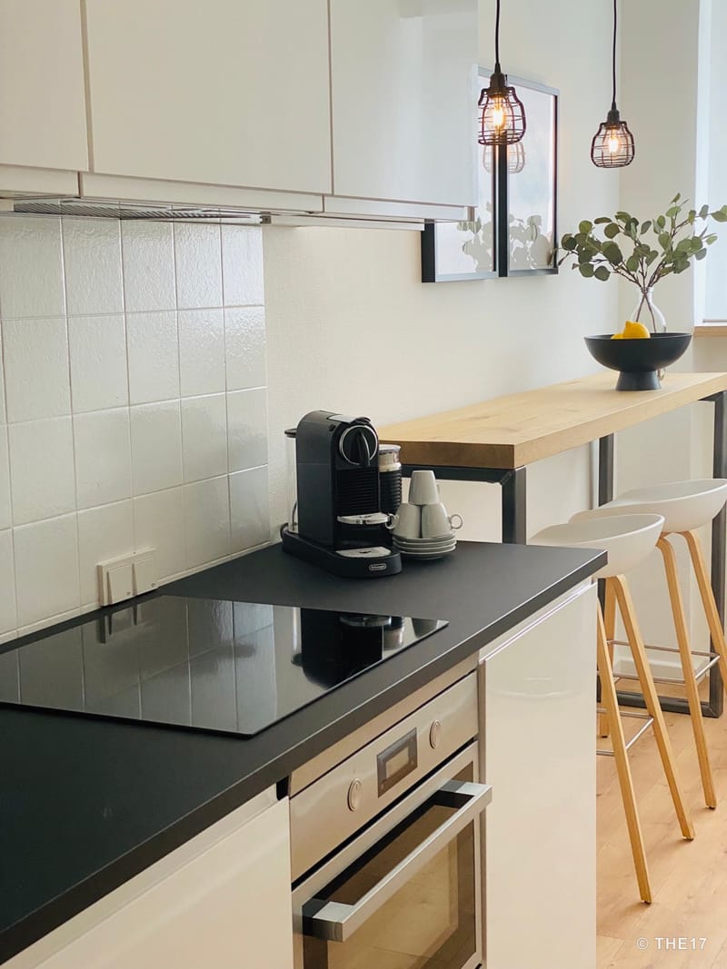 Modern kitchen with black countertop, induction cooktop, coffee machine, and wooden bar with two white stools.