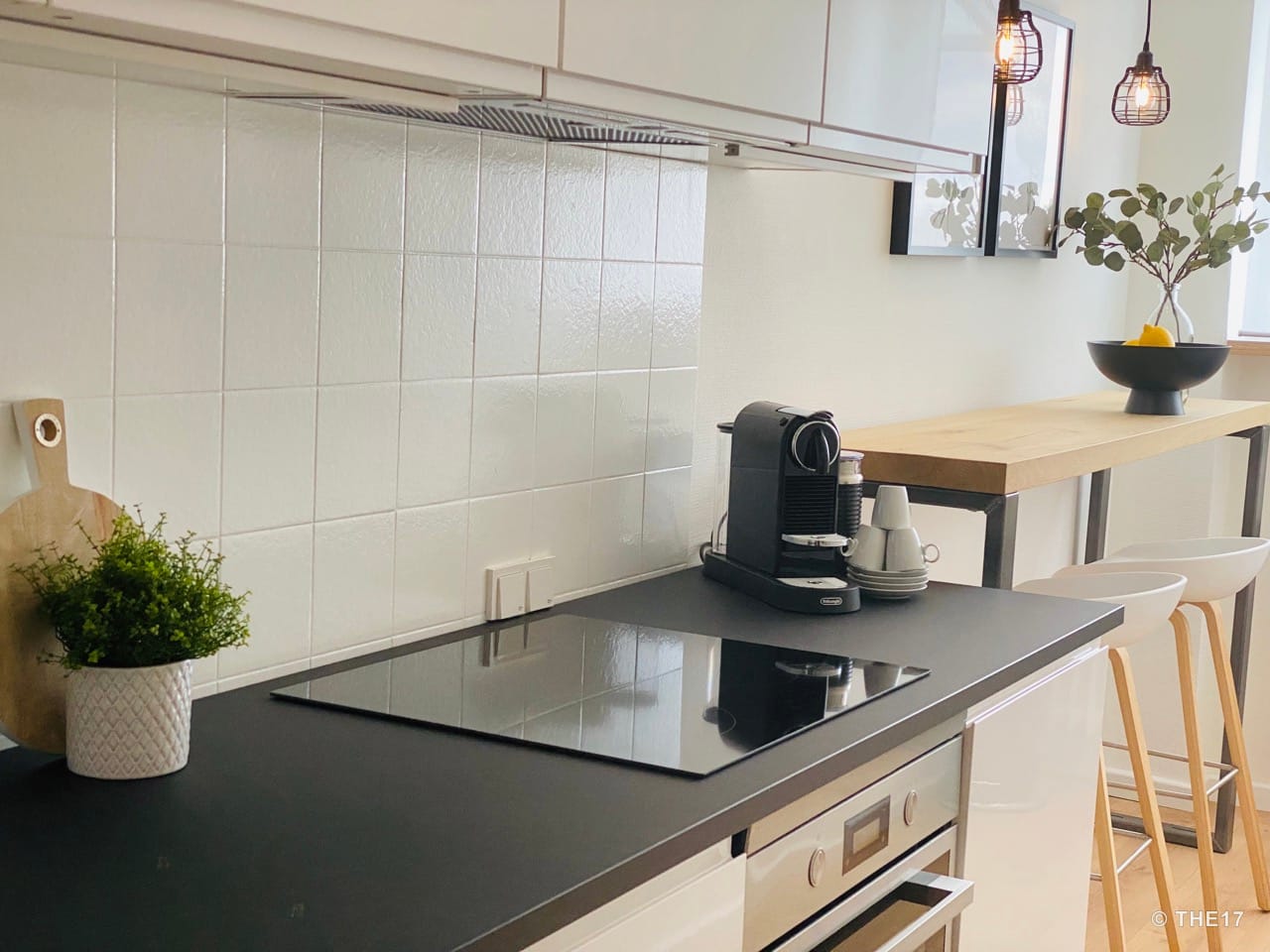 Modern kitchen with black countertop, ceramic hob, coffee machine, and wooden bar with stools.