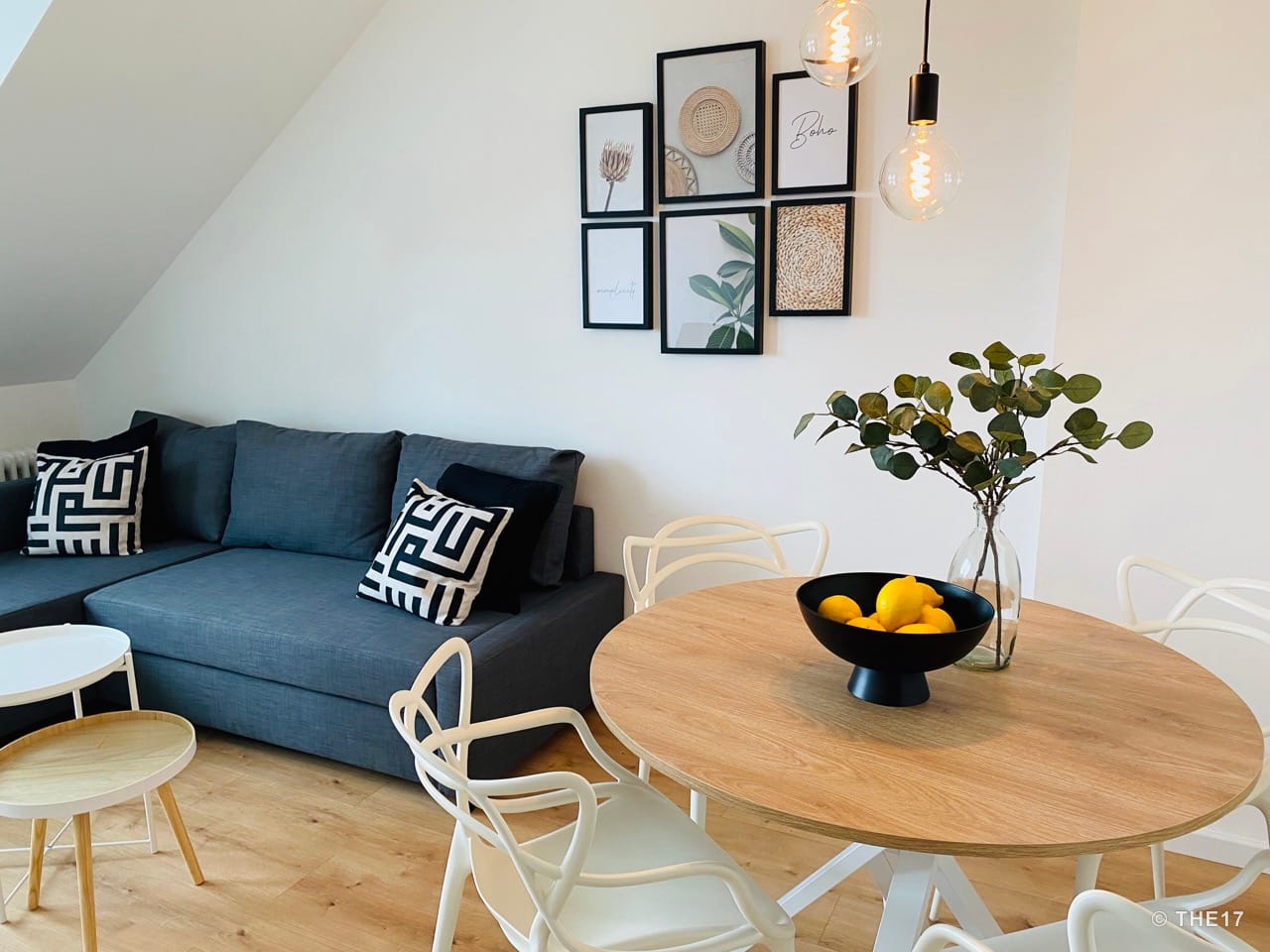 Living room with gray sectional sofa, round wooden table, white chairs, and framed wall art above sofa.