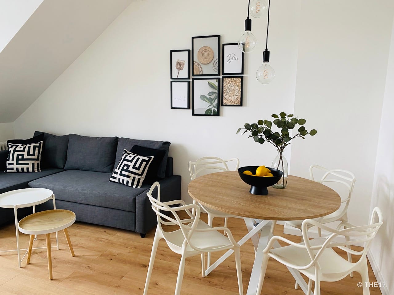 Living room with gray sectional sofa, round wooden table, white chairs, and modern wall art with framed pictures.