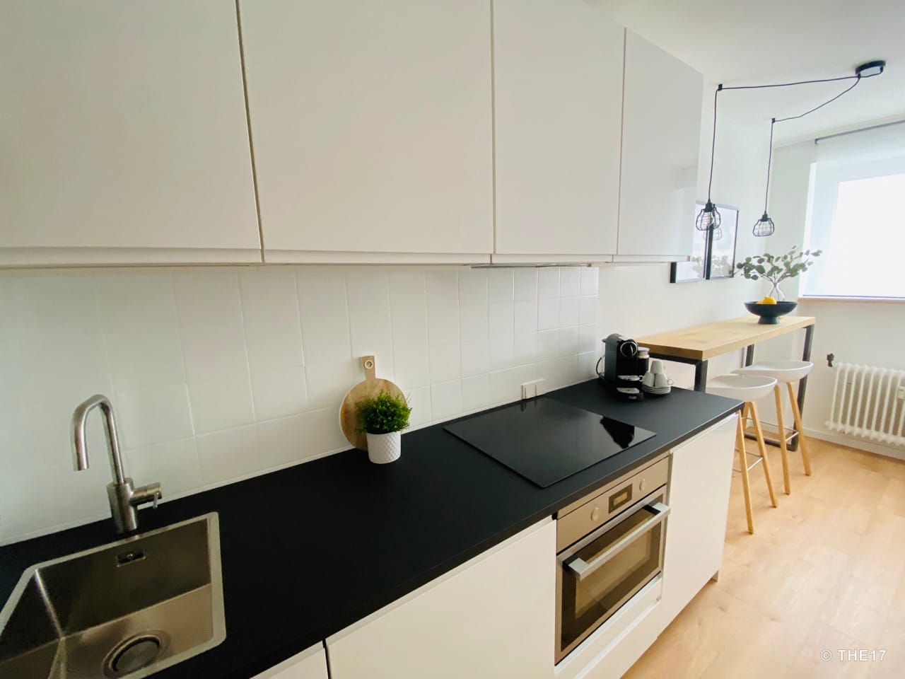 Modern kitchen with white cabinets, black countertop, sink, stove, oven and bar table with stools near window.